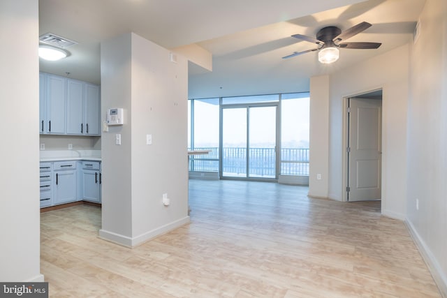 kitchen with expansive windows, white cabinets, ceiling fan, and light hardwood / wood-style flooring