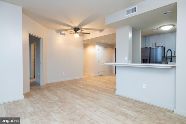 unfurnished living room featuring light wood-type flooring, sink, and ceiling fan