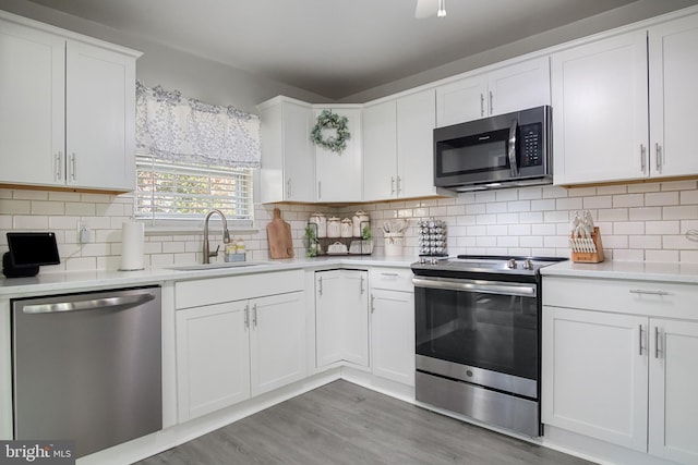 kitchen with sink, hardwood / wood-style flooring, appliances with stainless steel finishes, tasteful backsplash, and white cabinets