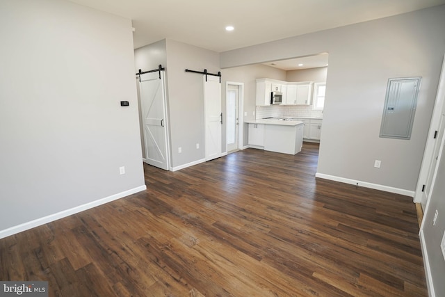 unfurnished living room with a barn door, dark wood-type flooring, and electric panel