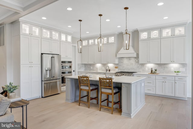 kitchen with an island with sink, appliances with stainless steel finishes, custom range hood, and white cabinets