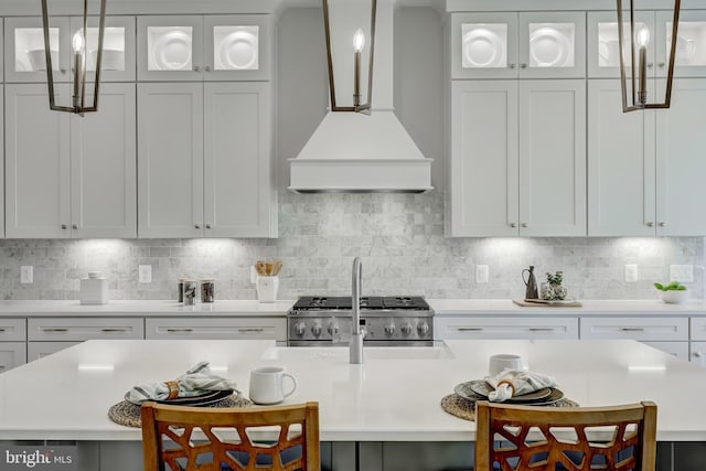 kitchen featuring a breakfast bar area, range, backsplash, white cabinets, and custom exhaust hood