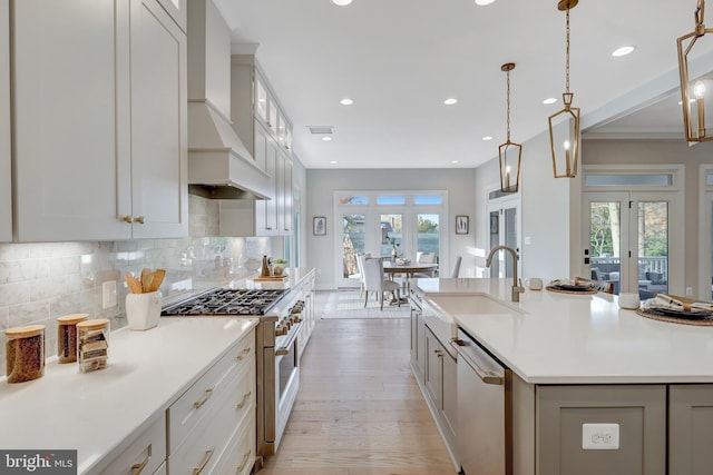 kitchen with premium range hood, decorative light fixtures, an island with sink, sink, and stainless steel appliances