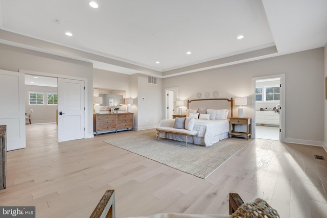 bedroom featuring ensuite bathroom, a tray ceiling, and light hardwood / wood-style floors