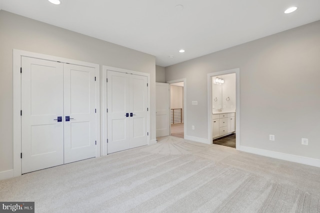 unfurnished bedroom with ensuite bathroom, light carpet, and two closets