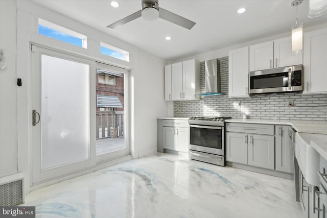 kitchen with pendant lighting, tasteful backsplash, ceiling fan, stainless steel appliances, and wall chimney range hood