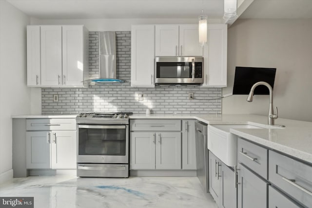 kitchen featuring wall chimney range hood, sink, hanging light fixtures, stainless steel appliances, and light stone counters