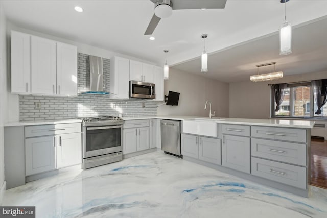 kitchen with wall chimney exhaust hood, sink, gray cabinetry, decorative light fixtures, and stainless steel appliances