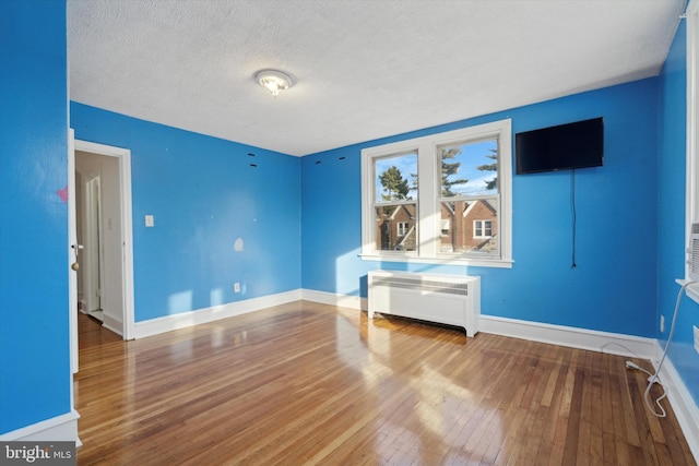 empty room featuring radiator heating unit, hardwood / wood-style floors, and a textured ceiling