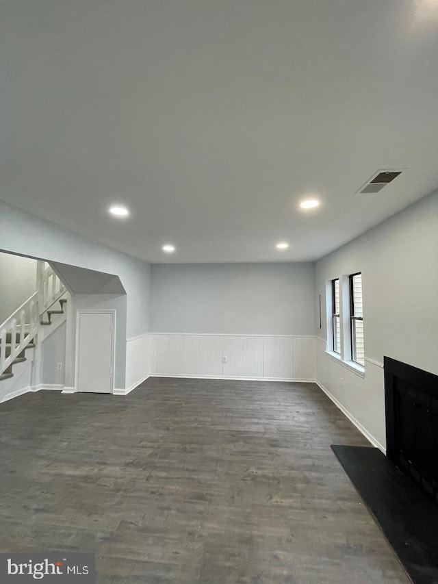 below grade area featuring a wainscoted wall, a fireplace, visible vents, stairway, and dark wood-style floors