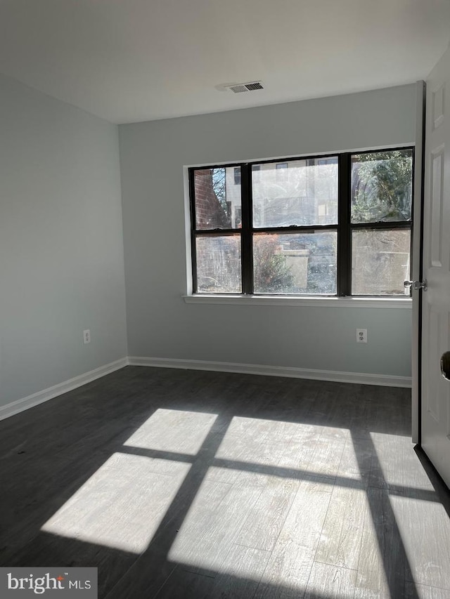 unfurnished room with dark wood-style flooring, visible vents, and baseboards