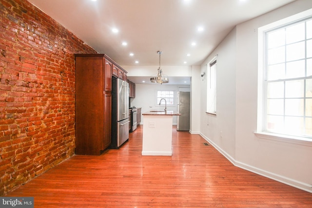 kitchen with sink, hanging light fixtures, stainless steel appliances, an island with sink, and light wood-type flooring