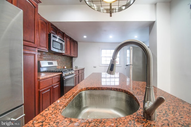 kitchen featuring stainless steel appliances, tasteful backsplash, sink, and dark stone countertops