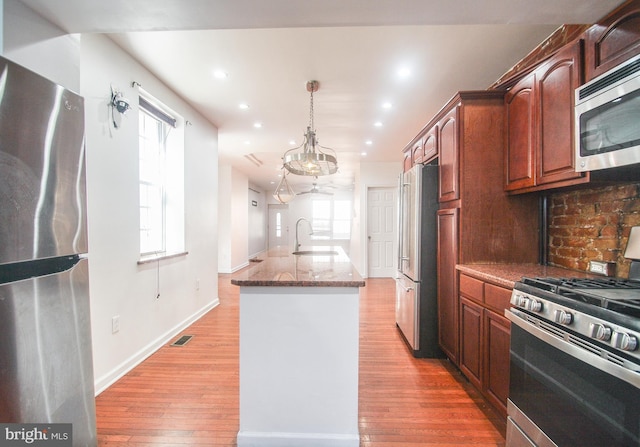 kitchen with appliances with stainless steel finishes, pendant lighting, sink, decorative backsplash, and light stone countertops