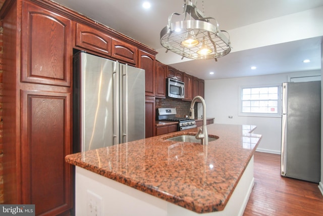 kitchen featuring stainless steel appliances, an island with sink, and light stone countertops