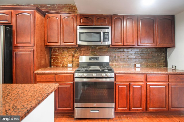 kitchen with tasteful backsplash, light stone countertops, stainless steel appliances, and light hardwood / wood-style floors