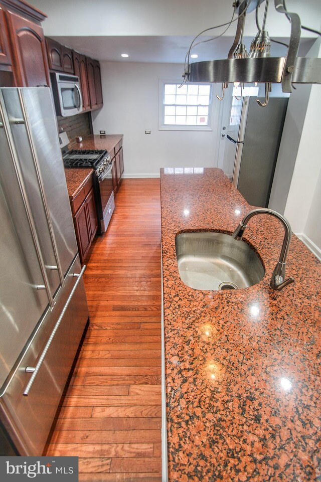 kitchen featuring appliances with stainless steel finishes, hardwood / wood-style floors, sink, dark stone countertops, and decorative backsplash