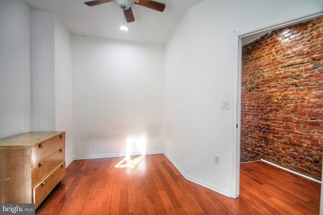 unfurnished room featuring ceiling fan, brick wall, and dark hardwood / wood-style floors