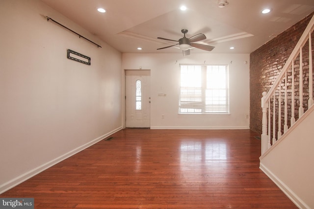 foyer entrance with ceiling fan, a tray ceiling, dark hardwood / wood-style flooring, and brick wall