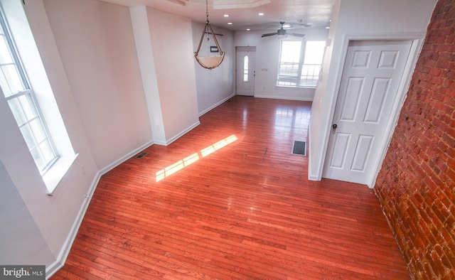 unfurnished dining area featuring wood-type flooring, ceiling fan, and brick wall