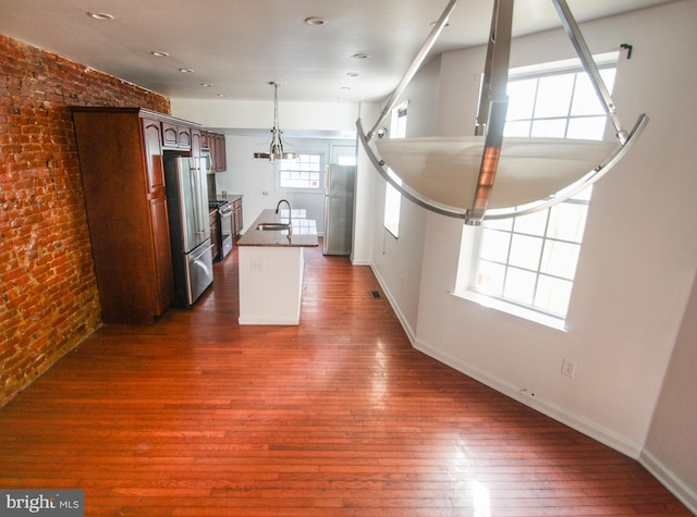 kitchen featuring high end refrigerator, stainless steel refrigerator, dark hardwood / wood-style flooring, brick wall, and a kitchen island with sink