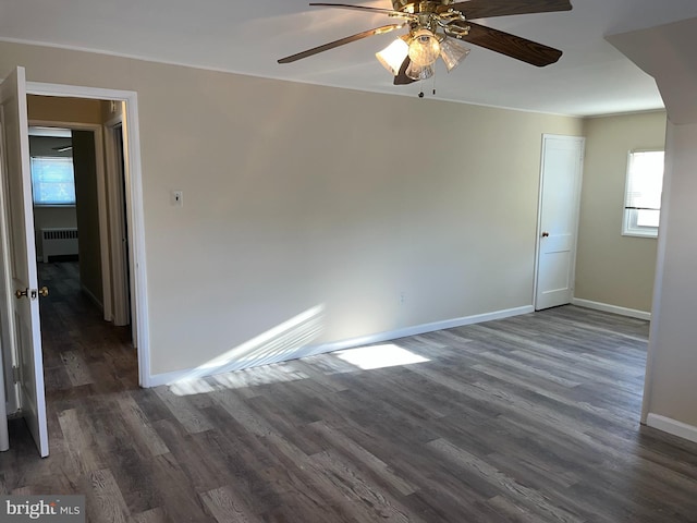 empty room with dark hardwood / wood-style floors, radiator heating unit, and ceiling fan