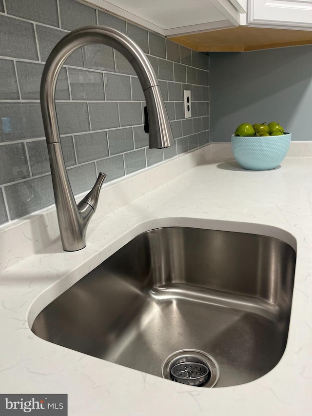 interior details featuring tasteful backsplash, sink, and white cabinets