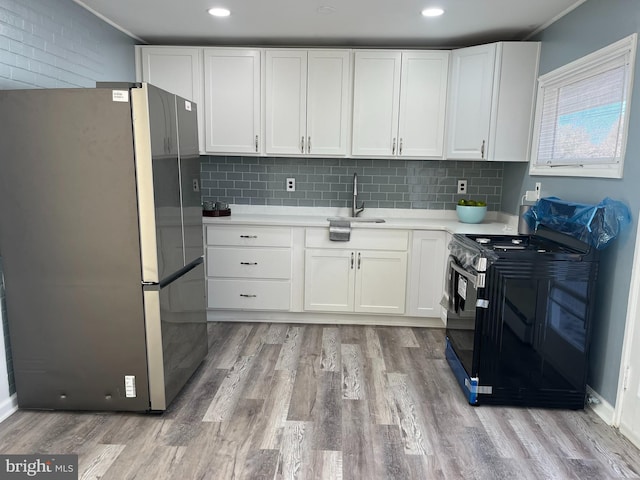 kitchen featuring black gas range oven, white cabinetry, sink, stainless steel fridge, and light hardwood / wood-style floors