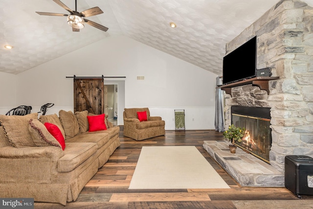 living room with vaulted ceiling, a fireplace, ceiling fan, a barn door, and dark wood-type flooring