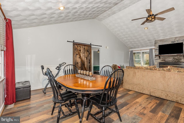 dining room featuring hardwood / wood-style flooring, vaulted ceiling, a barn door, and ceiling fan