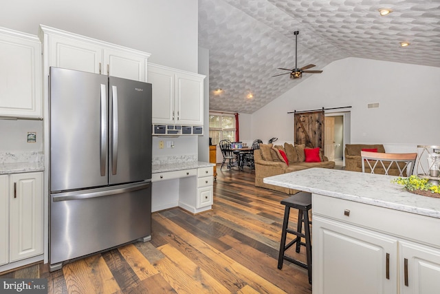 kitchen featuring stainless steel refrigerator, white cabinetry, a kitchen breakfast bar, a barn door, and dark wood-type flooring