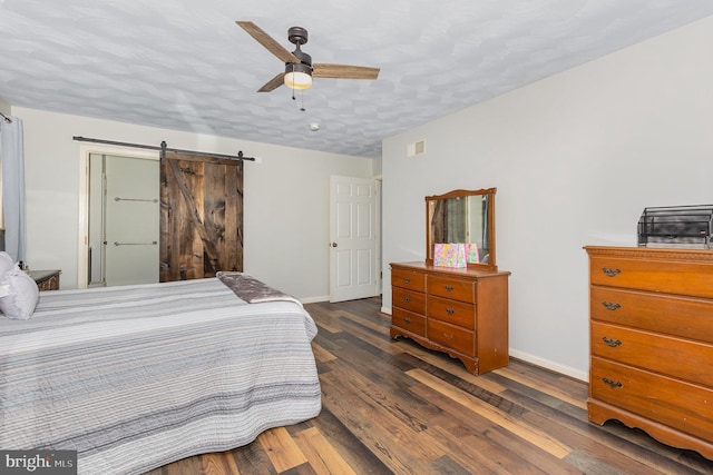 bedroom with dark hardwood / wood-style flooring, ceiling fan, a barn door, and a textured ceiling