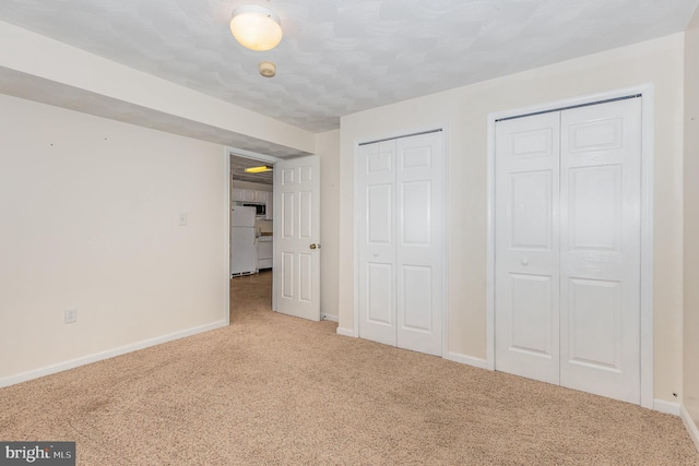 unfurnished bedroom with carpet floors, multiple closets, and white fridge