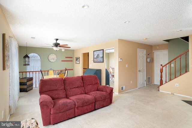 living room featuring visible vents, light carpet, a textured ceiling, and stairs