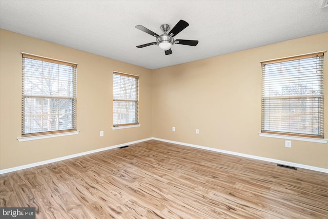 spare room with light wood-style floors, baseboards, visible vents, and a textured ceiling