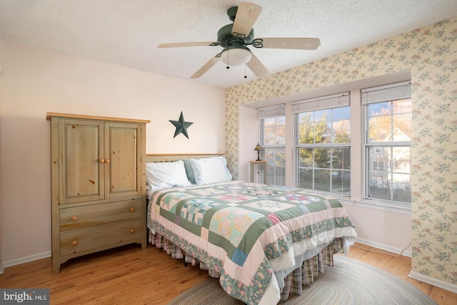 bedroom featuring a textured ceiling, light wood-style flooring, baseboards, and wallpapered walls