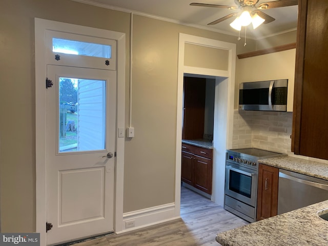 interior space featuring appliances with stainless steel finishes, backsplash, ornamental molding, light stone counters, and light hardwood / wood-style flooring