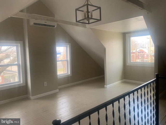 additional living space with lofted ceiling, a wall mounted AC, and light hardwood / wood-style flooring