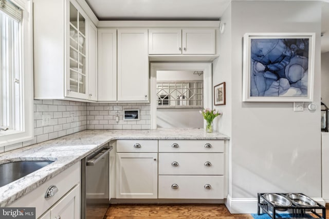 kitchen with dishwasher, tasteful backsplash, wood-type flooring, light stone countertops, and white cabinets