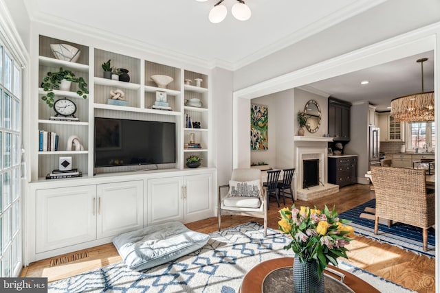 living room with sink, crown molding, light hardwood / wood-style flooring, and a chandelier