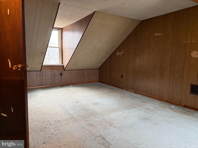 additional living space featuring vaulted ceiling, light carpet, and wood walls