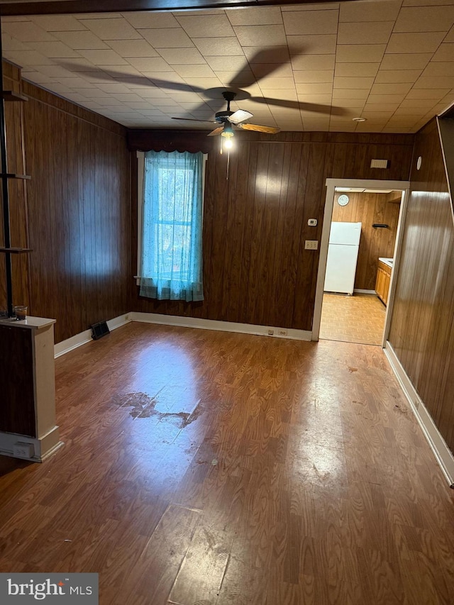 spare room featuring ceiling fan, wooden walls, and light wood-type flooring