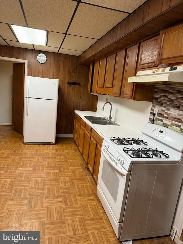 kitchen with a paneled ceiling, wooden walls, sink, light parquet flooring, and white appliances