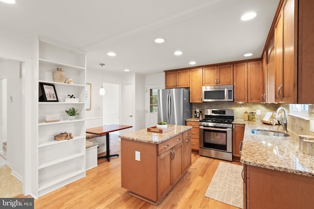 kitchen with pendant lighting, sink, stainless steel appliances, light stone countertops, and a kitchen island