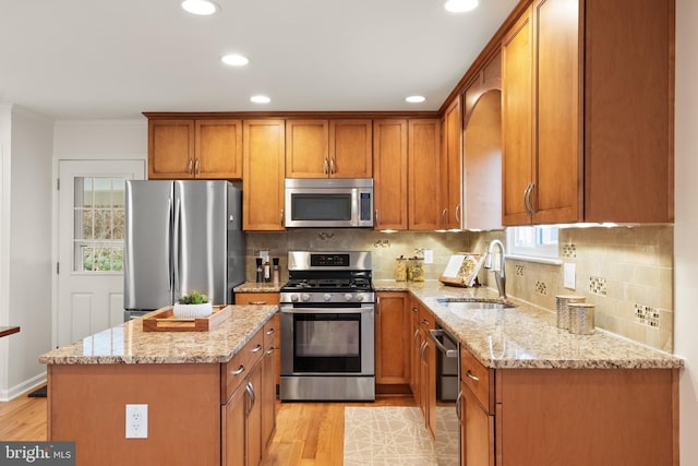 kitchen featuring sink, appliances with stainless steel finishes, a center island, light stone counters, and light wood-type flooring