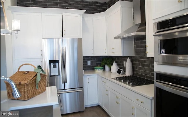 kitchen with wall chimney exhaust hood, white cabinetry, pendant lighting, stainless steel appliances, and backsplash