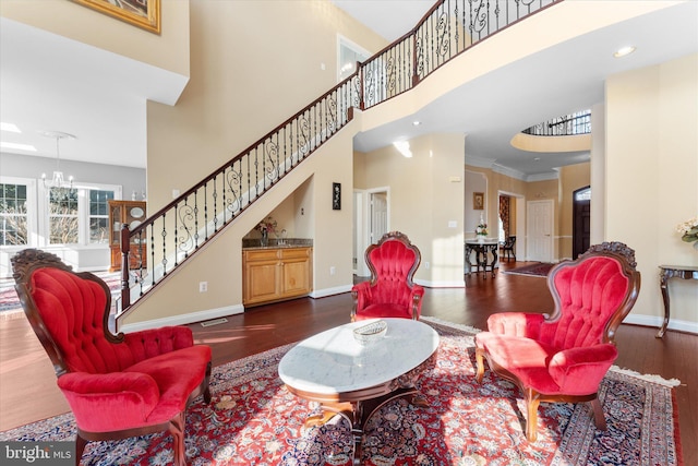 living area with baseboards, stairway, wood finished floors, an inviting chandelier, and a high ceiling