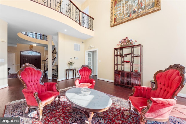 living room with wood finished floors, a towering ceiling, visible vents, stairs, and baseboards