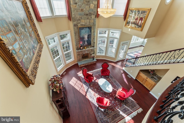 living room with a fireplace, wood finished floors, a towering ceiling, stairs, and an inviting chandelier