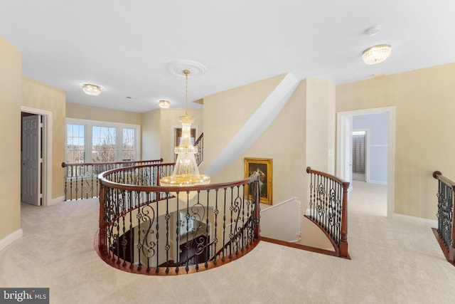 corridor with carpet floors, baseboards, a notable chandelier, and an upstairs landing